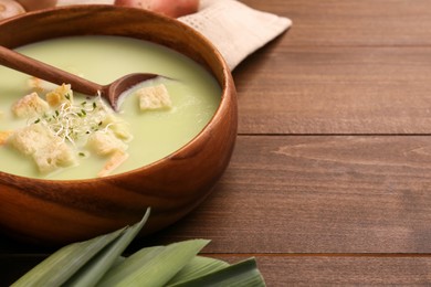 Photo of Bowl of tasty leek soup with croutons and spoon on wooden table, closeup. Space for text