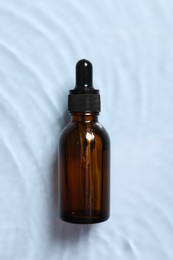 Photo of Bottle of cosmetic serum and water on light blue background, top view