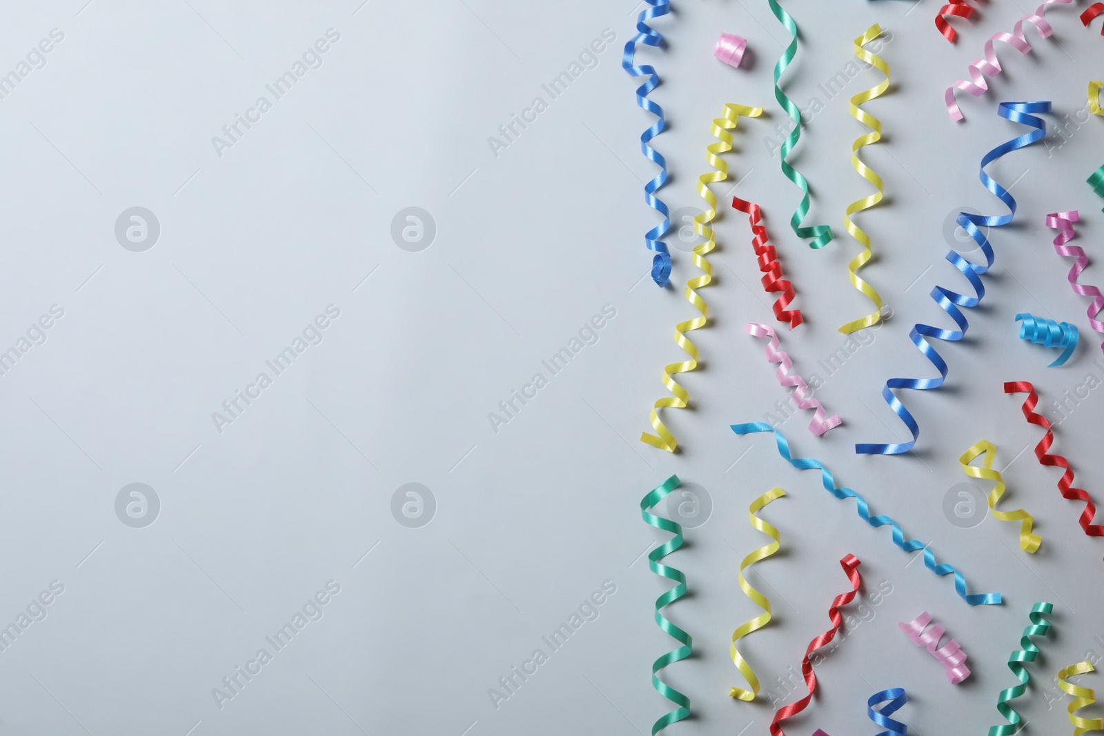 Photo of Colorful serpentine streamers on light background, flat lay. Space for text