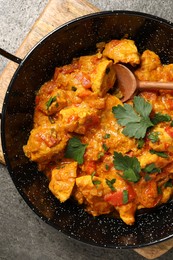 Delicious chicken curry in frying pan and spoon on grey table, top view