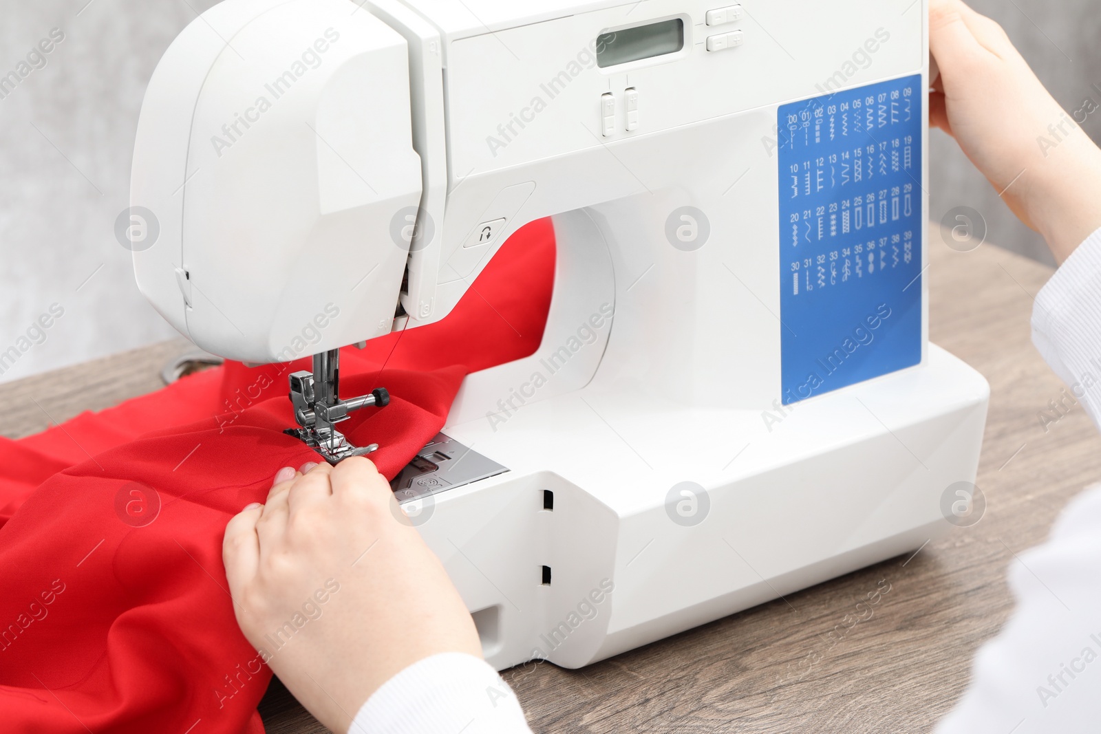 Photo of Seamstress working with sewing machine at wooden table indoors, closeup