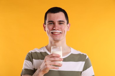 Happy man with milk mustache holding glass of tasty dairy drink on orange background