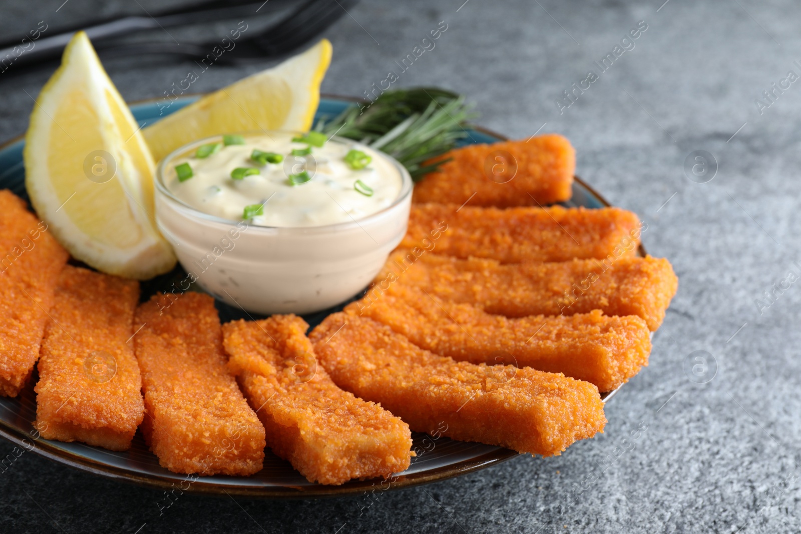 Photo of Fresh breaded fish fingers, sauce and lemon served on grey table, closeup