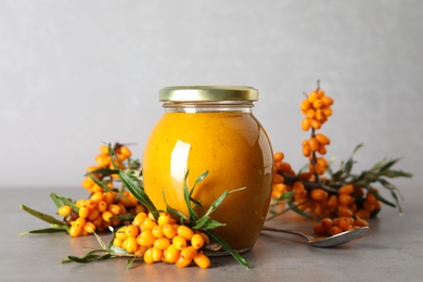 Photo of Delicious sea buckthorn jam and fresh berries on grey table