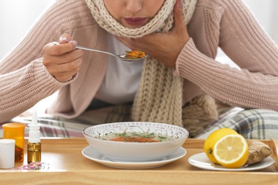 Photo of Sick young woman eating soup to cure flu at home, closeup