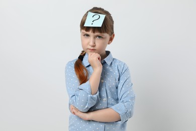 Photo of Pensive girl with question mark sticker on forehead against white background