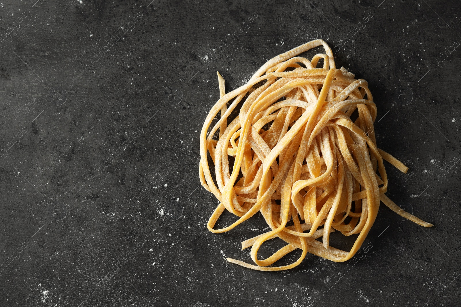 Photo of Uncooked homemade pasta on dark grey table, top view. Space for text