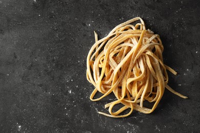 Photo of Uncooked homemade pasta on dark grey table, top view. Space for text