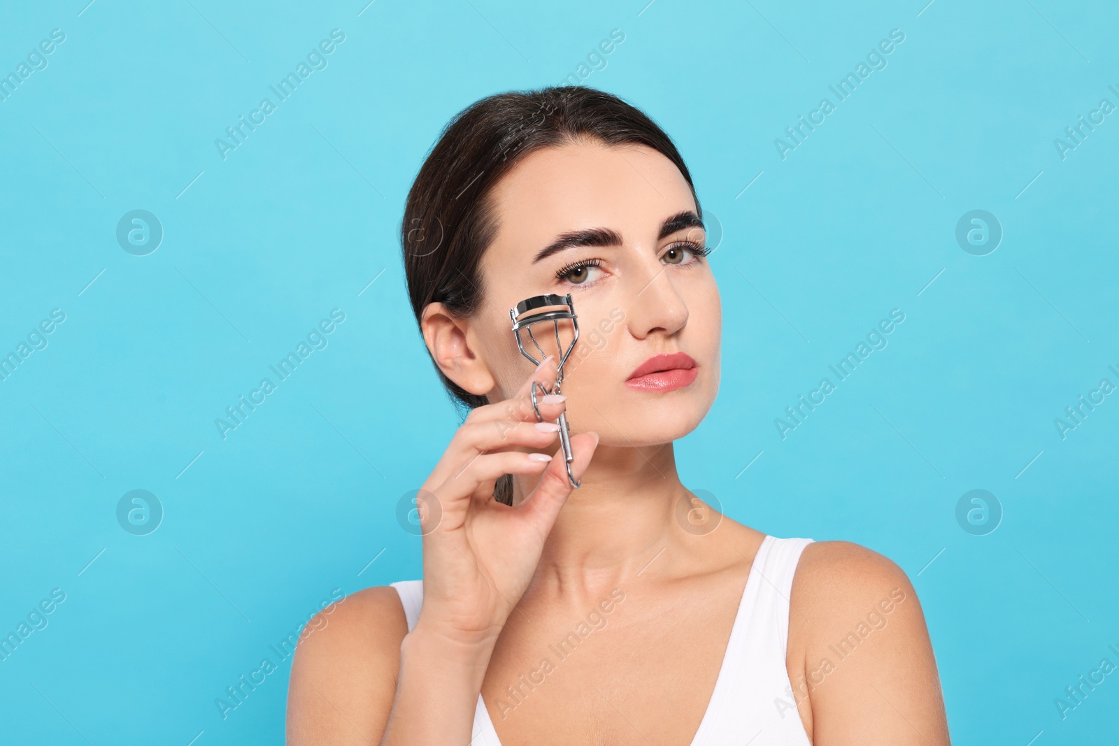 Photo of Woman using eyelash curler on turquoise background