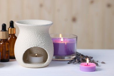 Different aromatherapy products, burning candles and lavender flowers on white wooden table, closeup