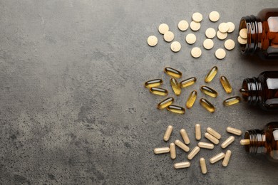 Overturned bottles with different dietary supplements on grey table, flat lay. Space for text