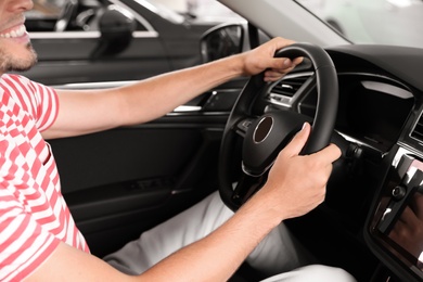 Happy man testing new car in salon