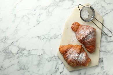 Photo of Tasty croissants with powdered sugar on white marble table, top view. Space for text