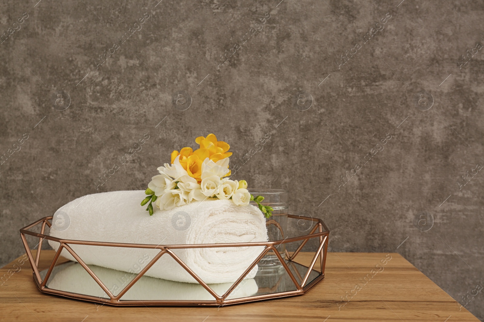 Photo of Rolled soft towel with beautiful flower in decorative tray on table. Space for text