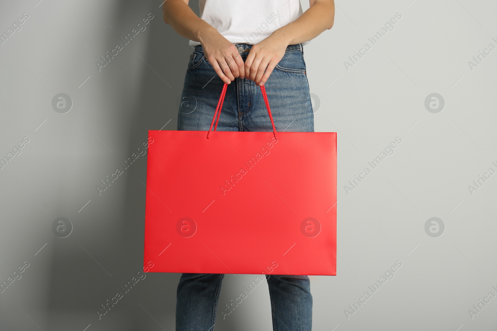 Photo of Woman with paper shopping bag on light grey background, closeup