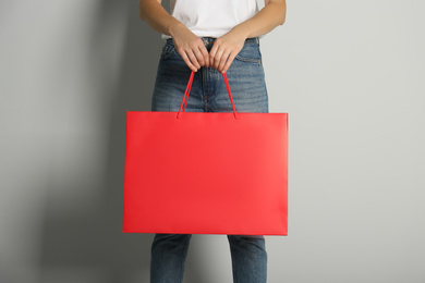 Photo of Woman with paper shopping bag on light grey background, closeup