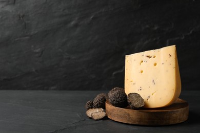 Photo of Wooden board with delicious cheese and fresh truffles on black table. Space for text
