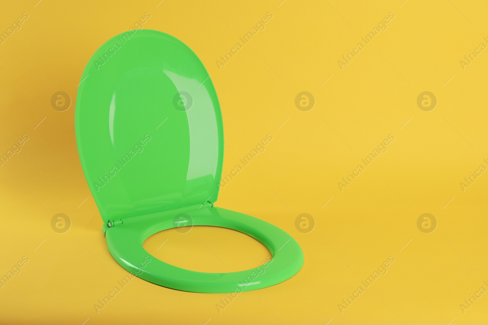 Photo of New green plastic toilet seat on yellow background, space for text