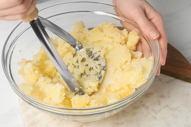 Woman making mashed potato at white table, closeup