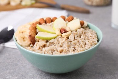 Photo of Bowl of delicious oatmeal with fruits and nuts on grey table