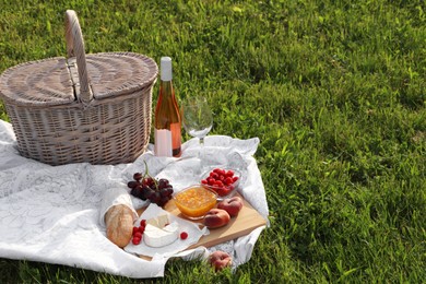 Picnic blanket with tasty food, basket and cider on green grass outdoors