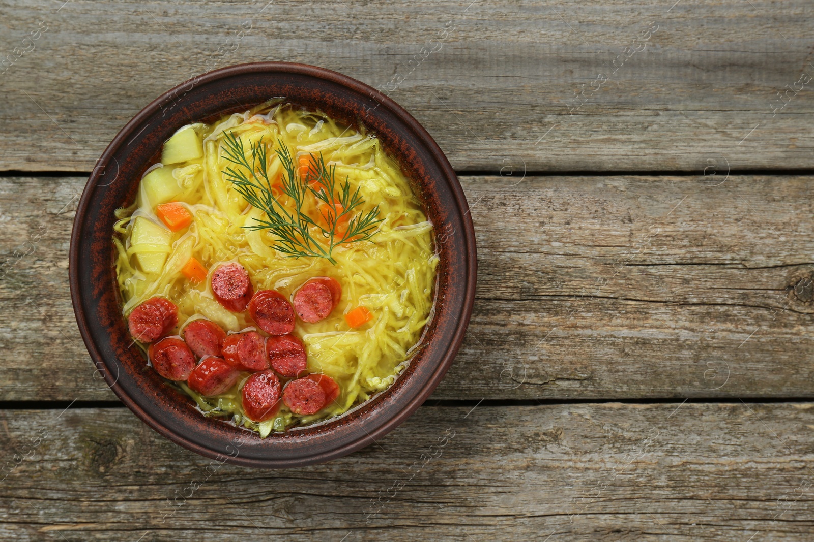 Photo of Bowl of delicious sauerkraut soup with smoked sausages and dill on old wooden table, top view. Space for text