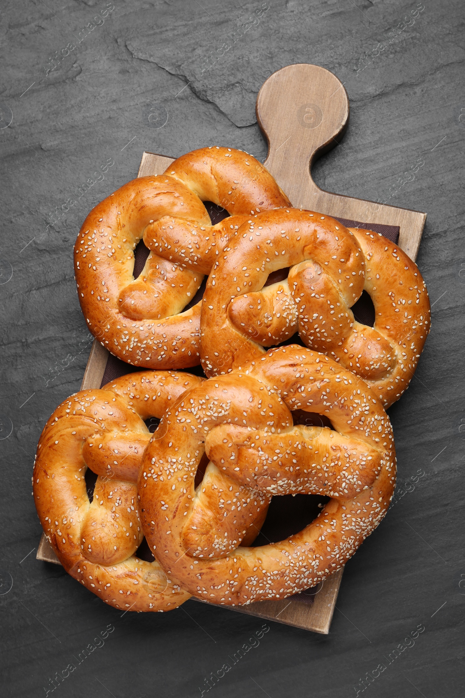 Photo of Delicious pretzels with sesame seeds on black table, top view