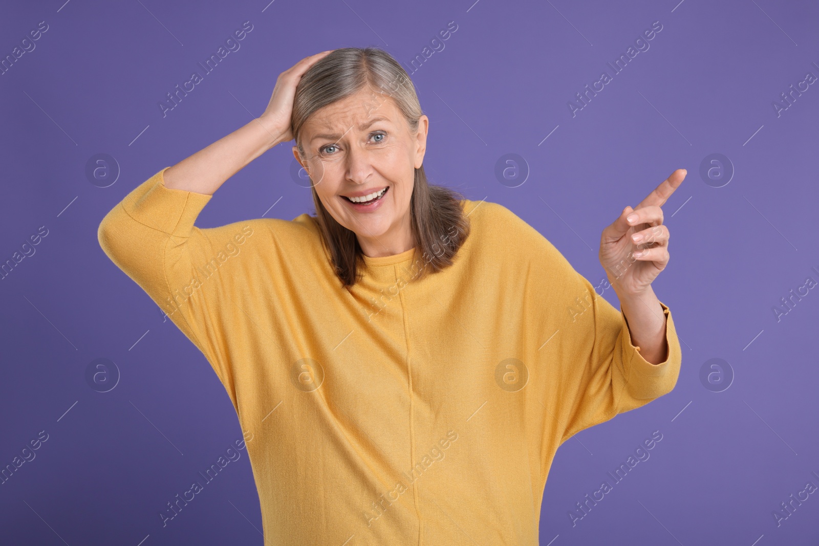 Photo of Surprised senior woman pointing at something on violet background