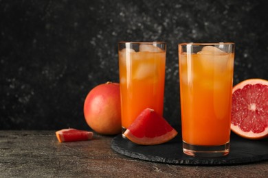 Photo of Tasty grapefruit drink with ice in glasses and fresh fruits on dark textured table. Space for text