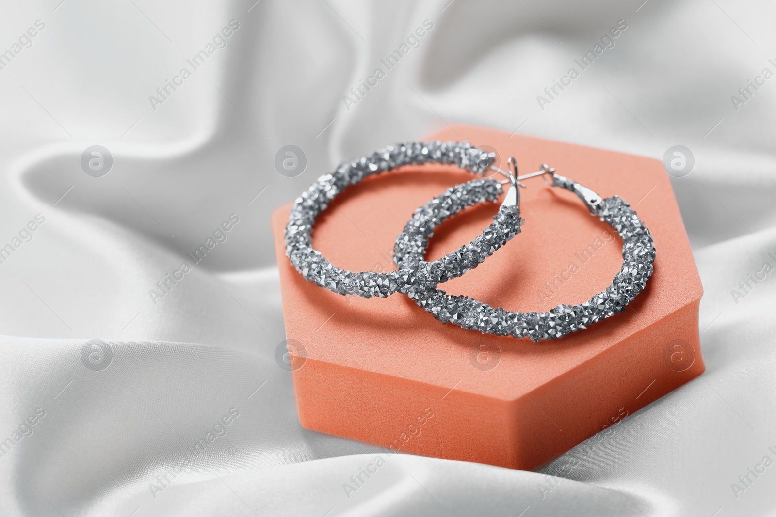 Photo of Beautiful earrings on orange podium. Luxury jewelry