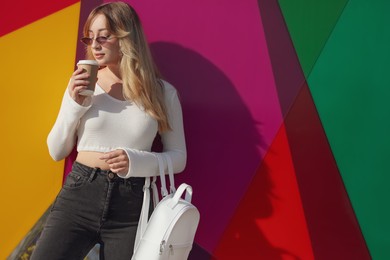 Photo of Young woman with stylish backpack and hot drink near color wall, space for text