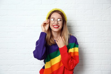 Beautiful young woman in warm sweater with hat near white brick wall