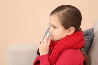 Photo of Cute little girl holding nasal spray on sofa indoors, space for text