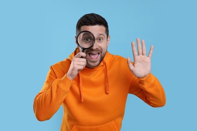 Photo of Happy man looking through magnifier glass on light blue background