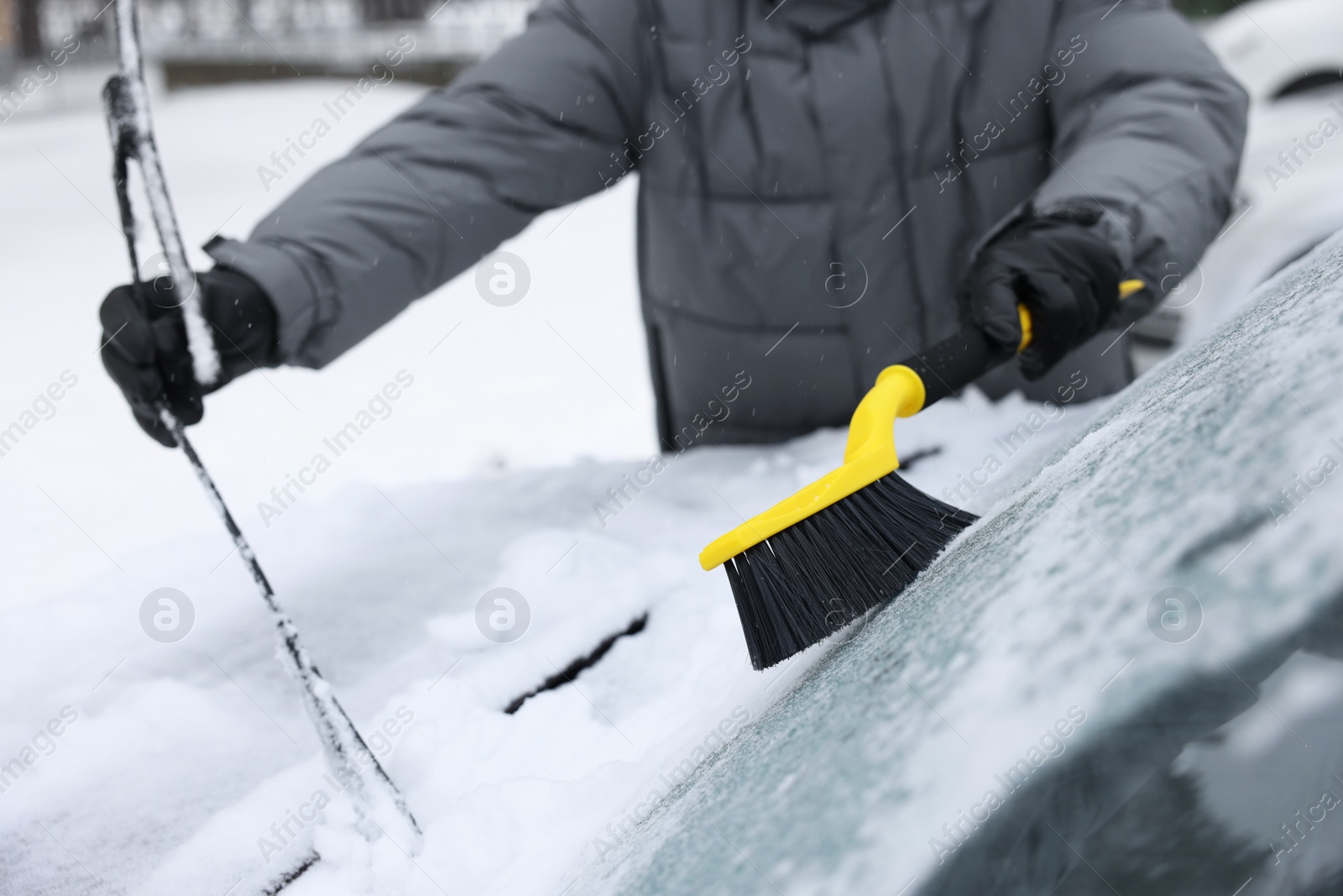 Photo of Man cleaning snow from car windshield outdoors, closeup