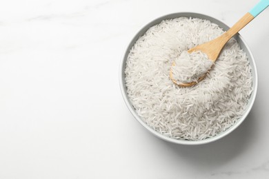 Photo of Raw basmati rice with spoon in bowl on white marble table, top view. Space for text