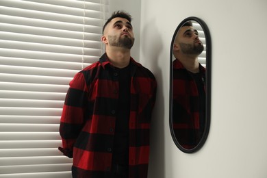 Photo of Sad young man near mirror at home