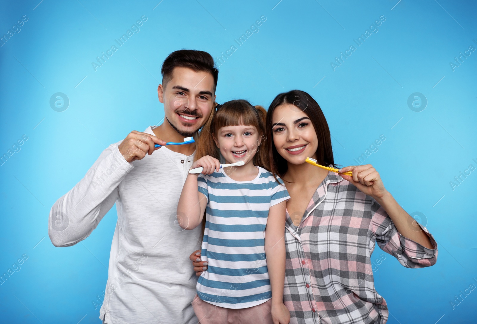 Photo of Little girl and her parents brushing teeth together on color background