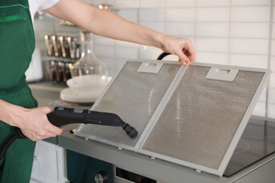 Photo of Professional janitor cleaning mesh filter of cooker hood in kitchen, closeup
