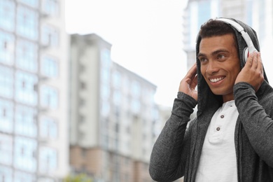 Handsome young African-American man with headphones listening to music on city street. Space for text