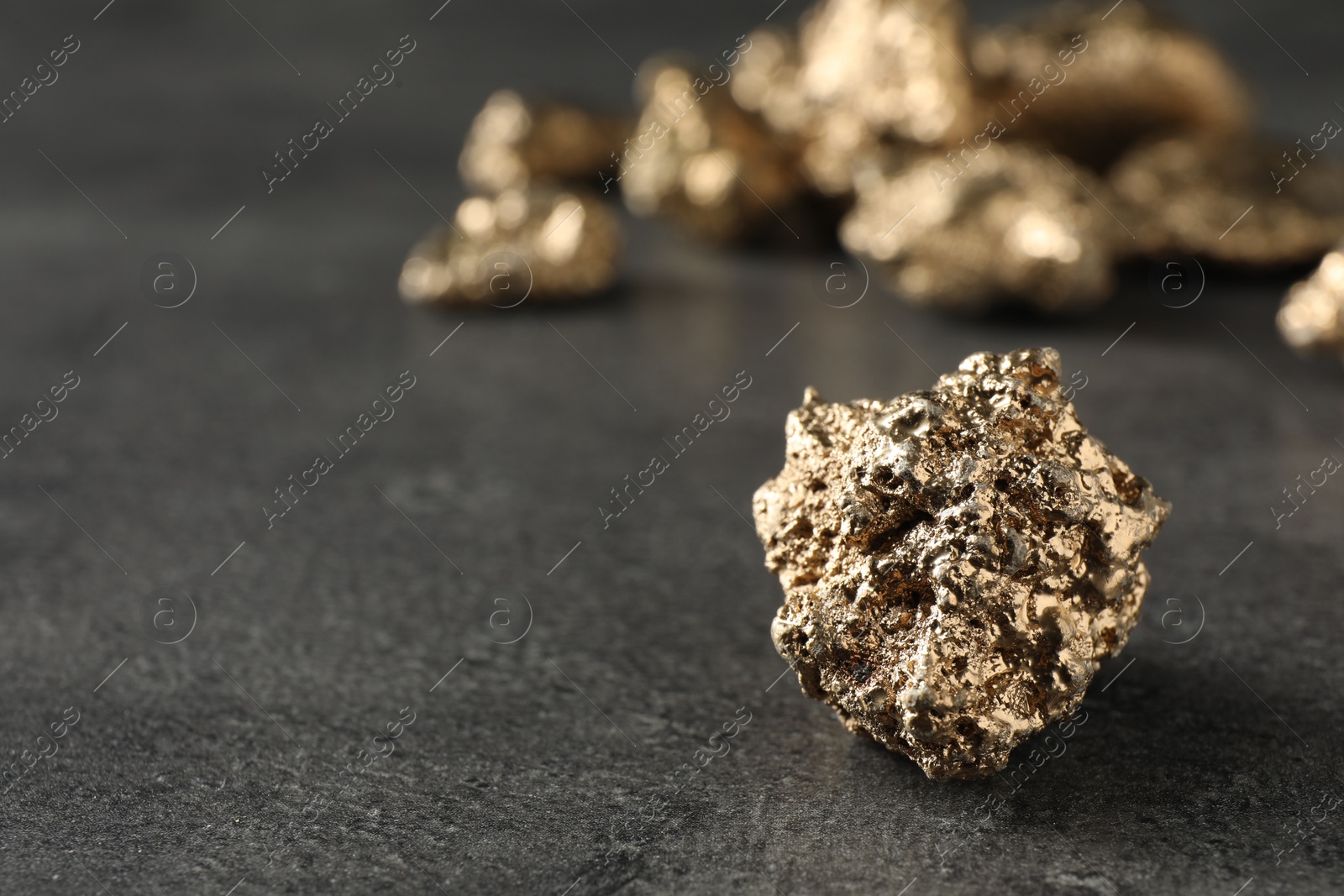 Photo of Shiny gold nugget on grey surface, closeup. Space for text