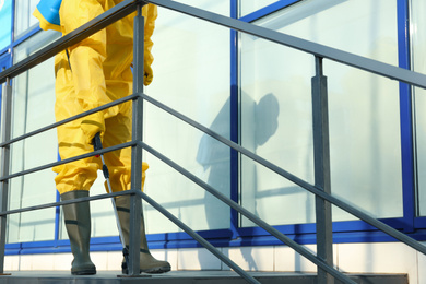 Photo of Male worker in protective suit spraying insecticide on stairs outdoors, closeup. Pest control