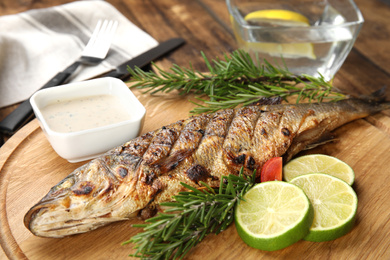 Photo of Delicious grilled fish with lime on wooden board, closeup