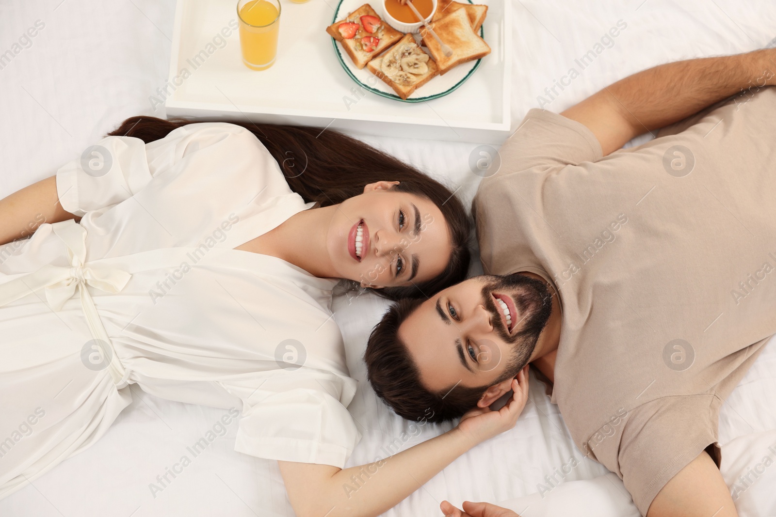 Photo of Happy couple lying on bed near white tray with breakfast, above view