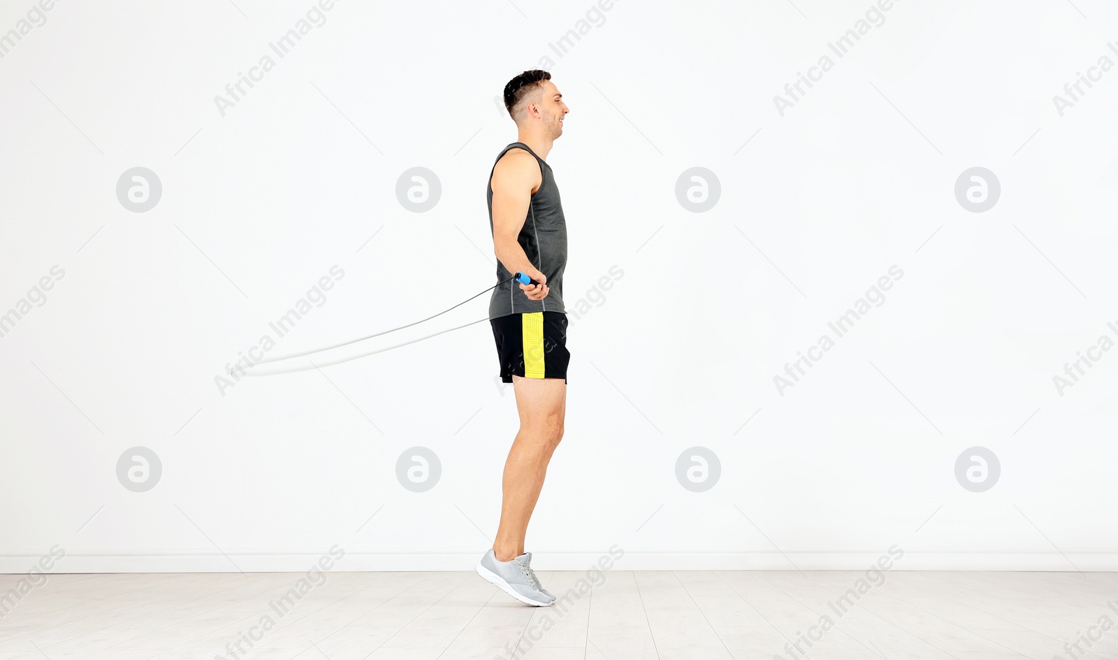 Photo of Young sportive man training with jump rope in light room