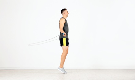Photo of Young sportive man training with jump rope in light room