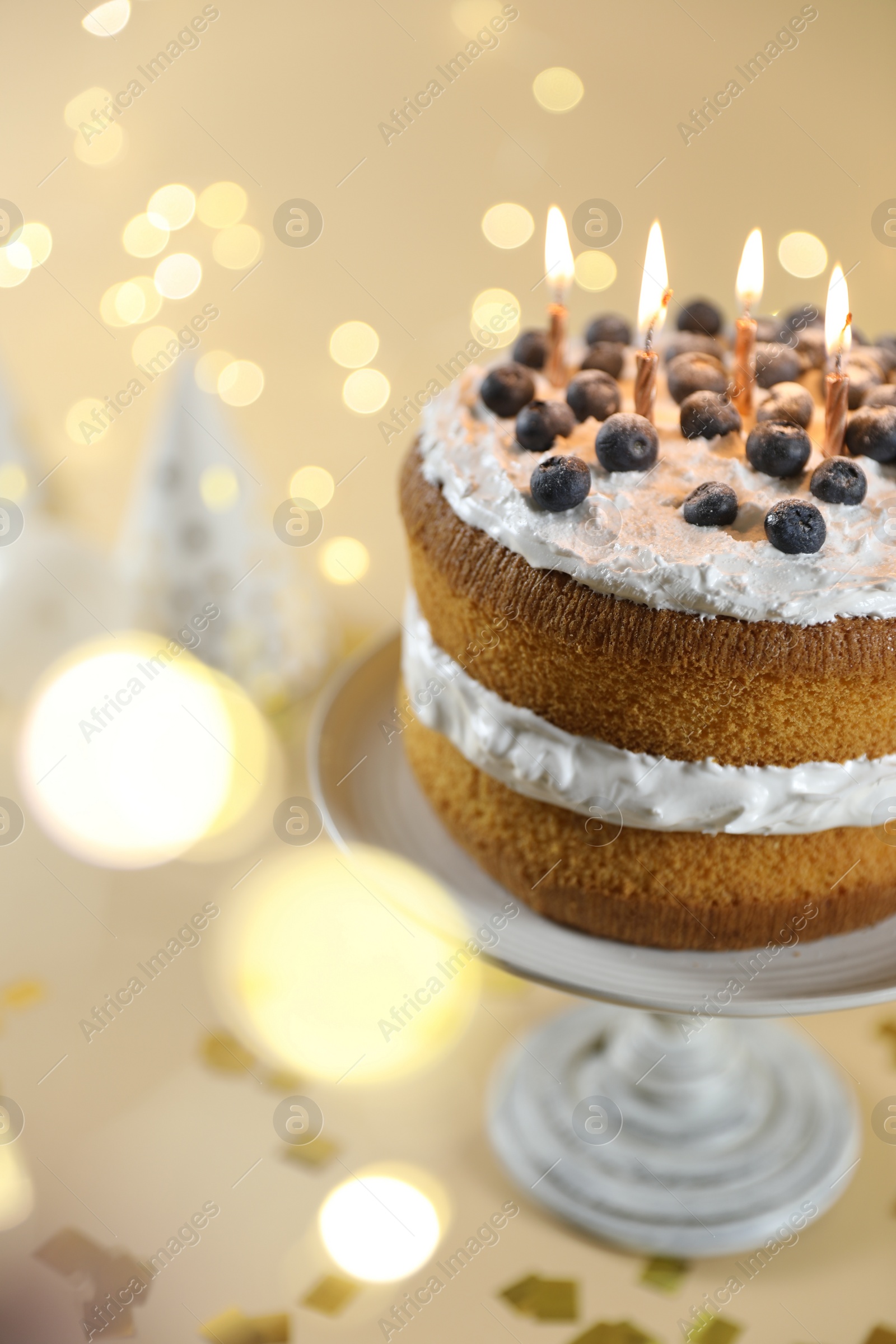 Photo of Tasty cake with burning candles on beige background against blurred lights