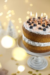 Photo of Tasty cake with burning candles on beige background against blurred lights