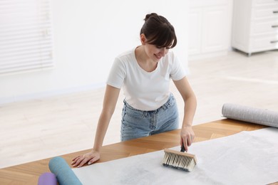 Photo of Woman applying glue onto wallpaper sheet at wooden table indoors