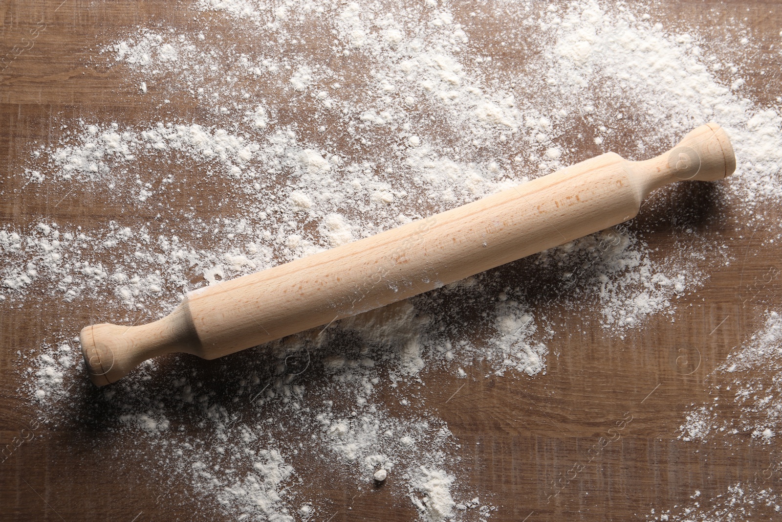 Photo of Scattered flour and rolling pin on wooden table, top view